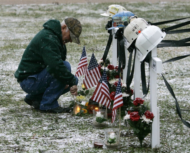 Image: A man lights candles at the base of crosses for four miners killed in the Sago Mine explosion in 2006