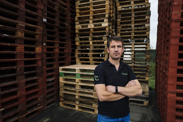 Image: Yumer Mustafa stands next to pallets used to transport fruit