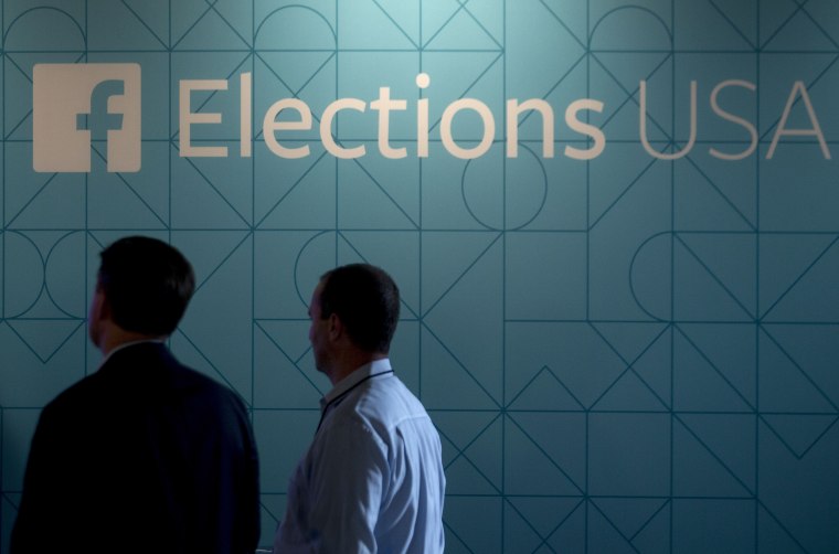 Image: Two men stand under a Facebook Elections USA sign at the first GOP primary debate