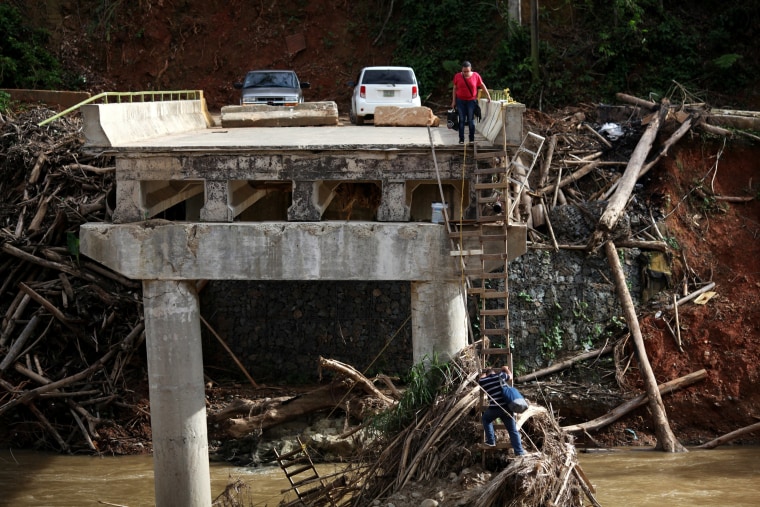 Image: A woman looks as her husband climbs down a ladder at a partially destroyed bridge, after Hurricane Maria hit the area in September, in Utuado