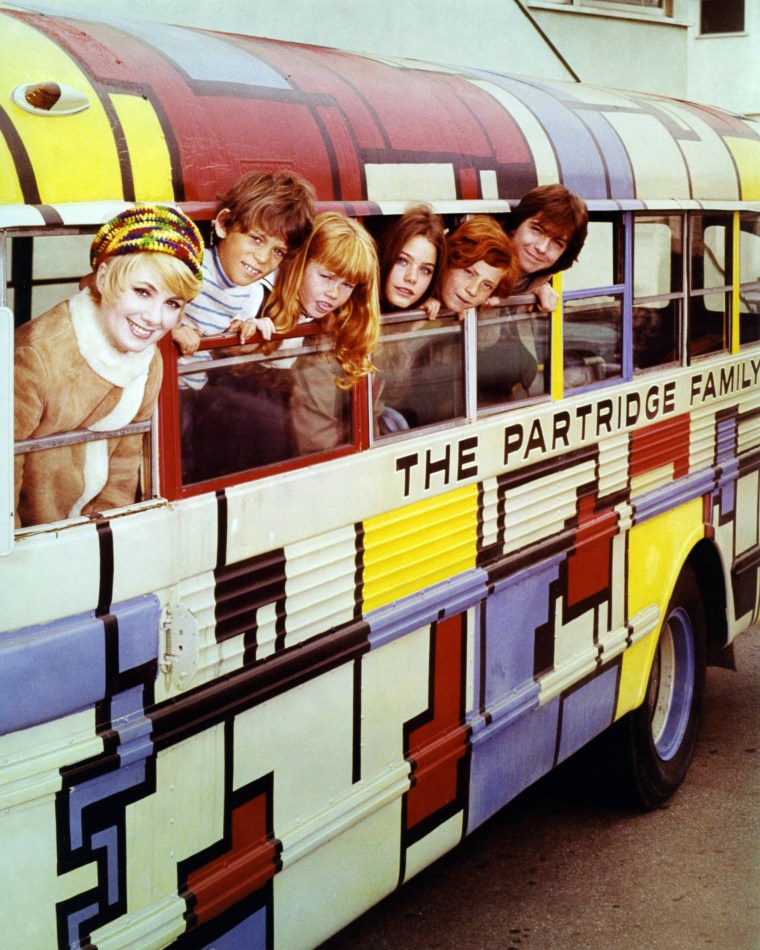 Image: Shirley Jones, Brian Forster, Suzanne Crough, Susan Dey, Danny Bonaduce and David Cassidy  pose leaning out of the windows of a bus