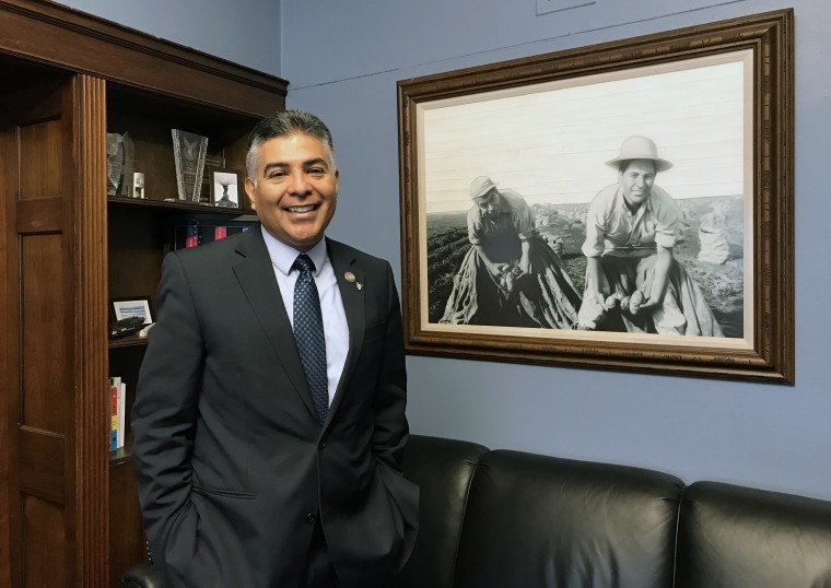 Image: Rep. Tony Cardenas, D-Calif., stands near a drawing of a photo of his father, smiling, and grandfather harvesting potatoes as farm workers