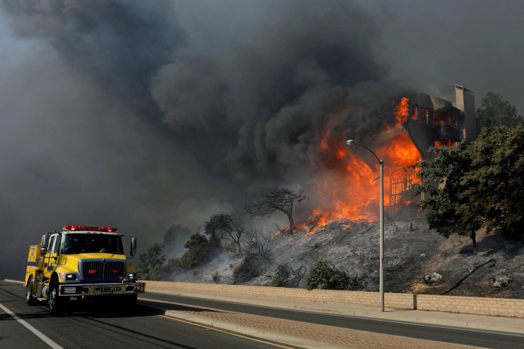 Image: FILE PHOTO: A fire crew passes a burning home during a wind-driven wildfire in Ventura, California