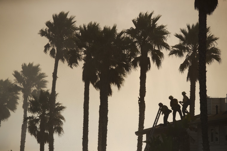 Firefighters stand on the rooftop of a beach house to water down the property while battling a wildfire at Faria State Beach in Ventura, on Dec. 7.