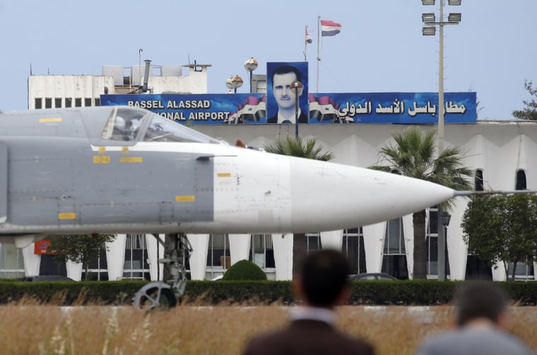 Image: A Russian Su-24 bomber passes by a portrait of Bashar al-Assad at Hemeimeem air base