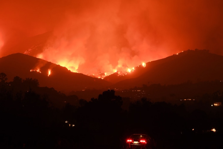 Image: A man sits in his car as he watches flames from the Thomas Fire in the hills of Montecito