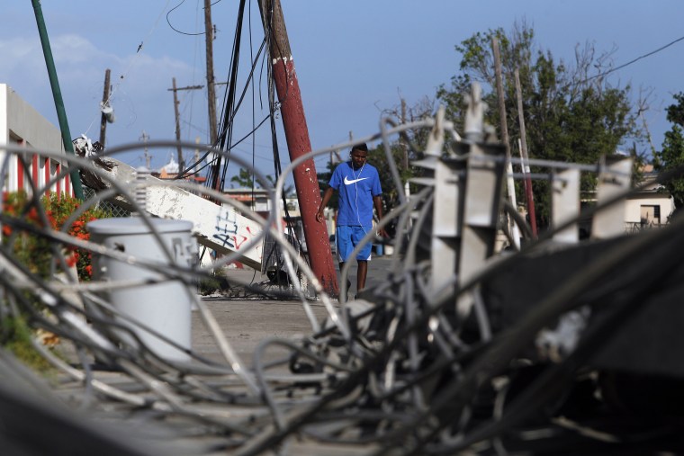 Image: A man walks past downed electricity poles in the Punta Santiago beachfront neighborhood in Humacao