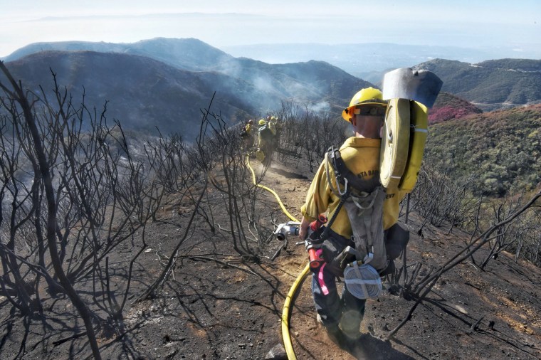 Image: Santa Barbara County Firefighters haul dozens of pounds of hose and equipment down steep terrain below E. Camino Cielo to root out and extinguish smoldering hot spots in Santa Barbara, California on Dec. 19, 2017.