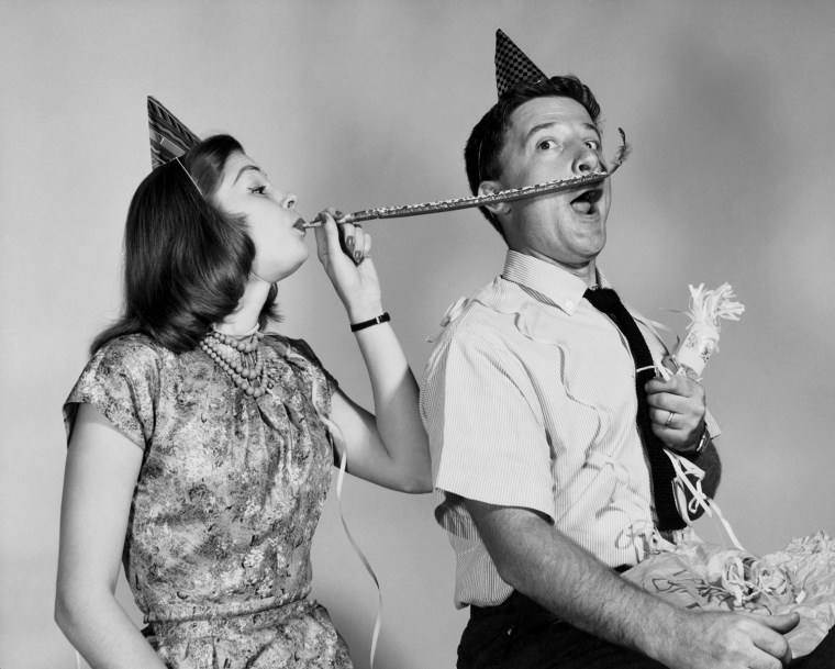 Young woman blowing a noisemaker near a young man's face. Photo by: Superstock/Everett Collection(255-28547)