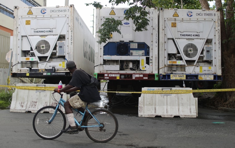 Image: A man bikes past refrigerated FEMA trailers