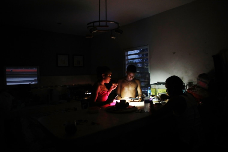 Image: Family members eat dinner at dusk with light from a cell phone