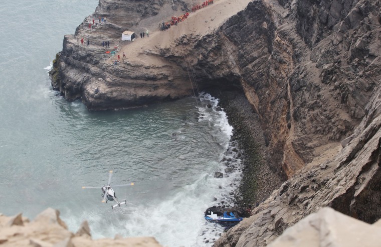 Image: A helicopter helps rescue workers at the scene after a bus crashed with a truck and careened off a cliff along a sharply curving highway north of Lima