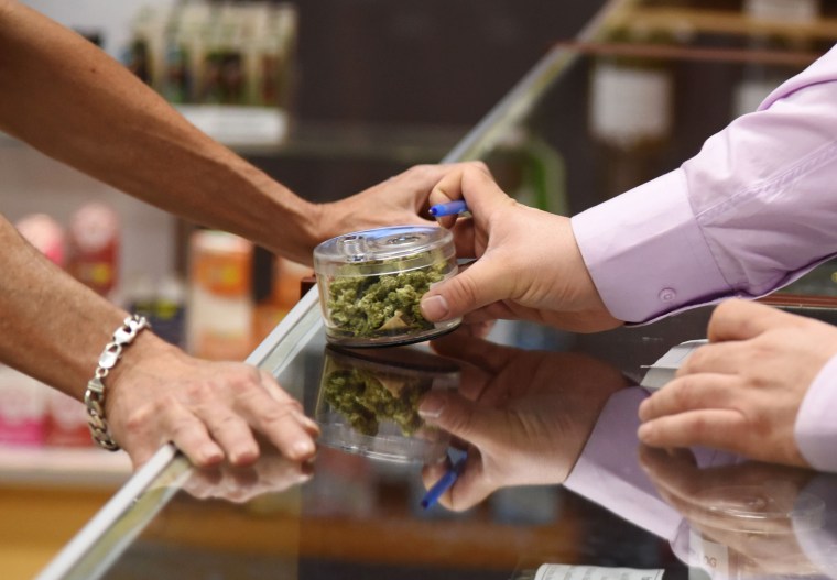 Image: A budtender shows cannabis buds to a customer at the Green Pearl Organics dispensary