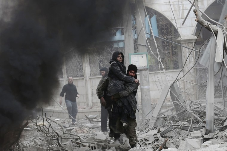 Image: A Syrian man carries an injured woman following air strikes