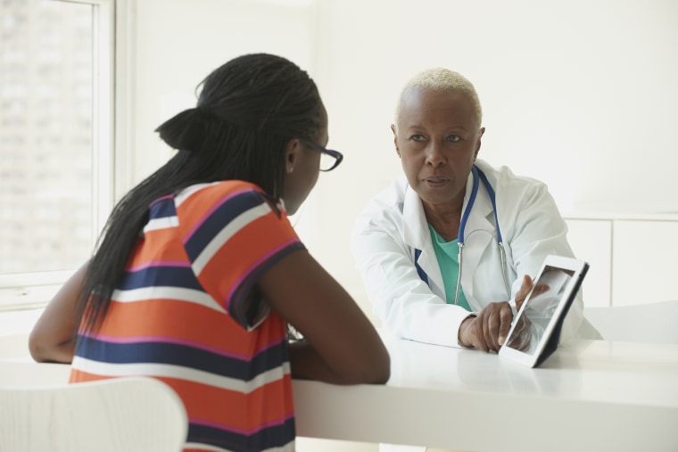 Image: Black doctor using digital tablet with patient