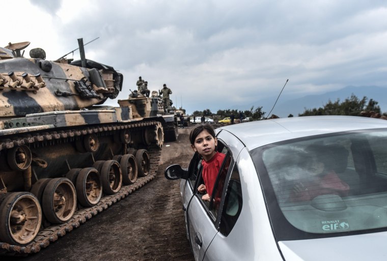 Image: A girl leans out of the window of a car to look as Turkish army tanks and soldiers gather close to the Syrian border