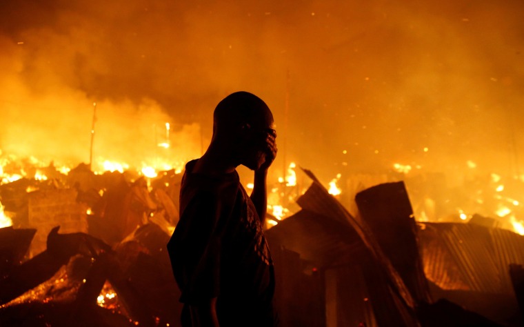 Image: A resident covers his face as he attempts to extinguish a fire that broke out at the Kijiji slums in Nairobi