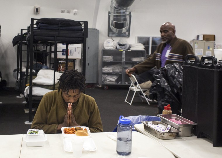 Image: Resident Derek Diamond, 31, prays before eating a second helping of dinner in a temporary shelter for the homeless