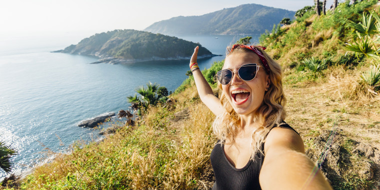 Young woman takes selfie, on hillside above sea