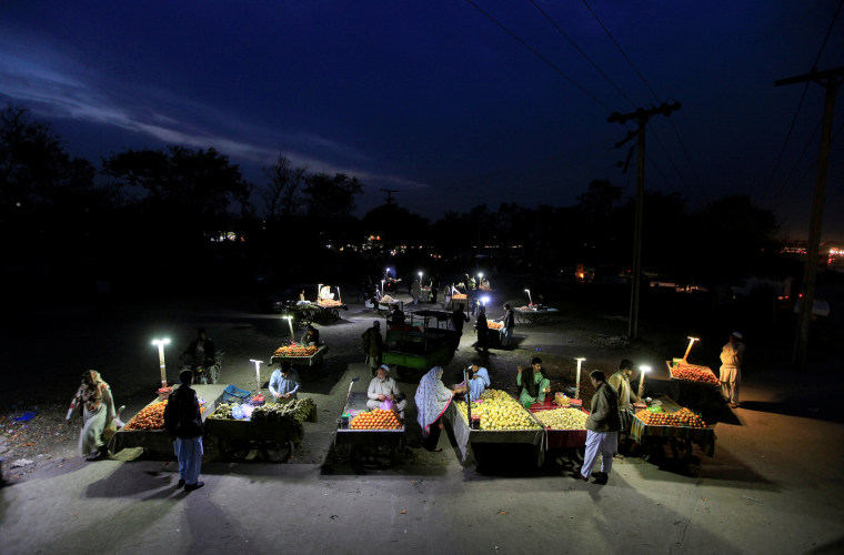 Image: Customers shop at an open air evening fruit market along a road in Rawalpindi