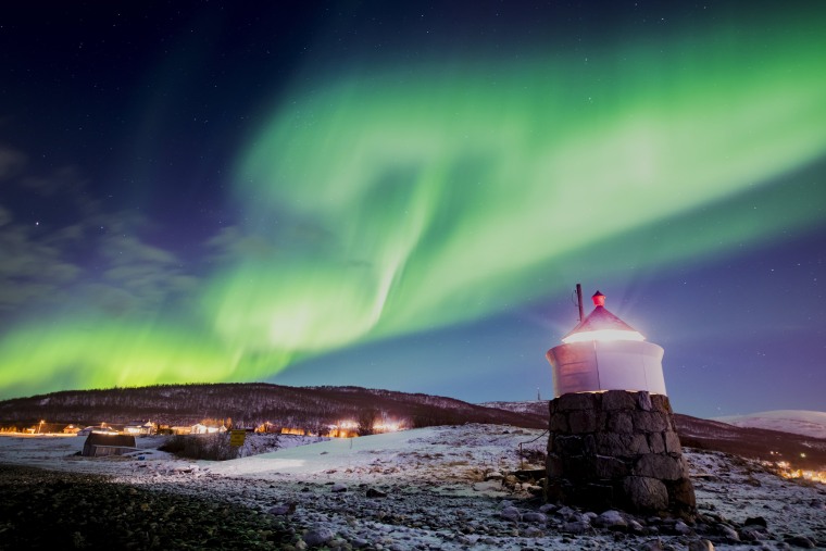 Image: Aurora borealis or northern lights are visible in the sky above a lighthouse to the village of Strand