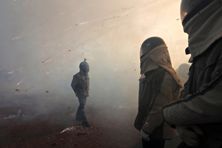 Image: Revelers wearing motorcycle helmets get sprayed by firecrackers