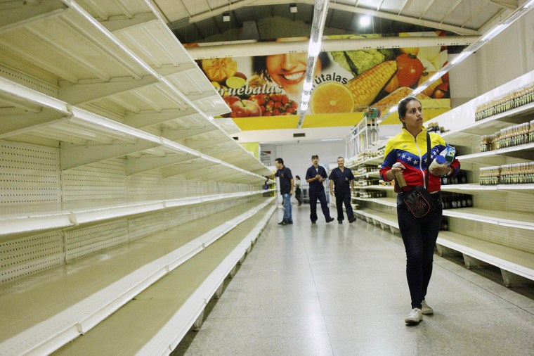 Image: A woman walks past empty shelves at a supermarket in San Cristobal, Venezuela