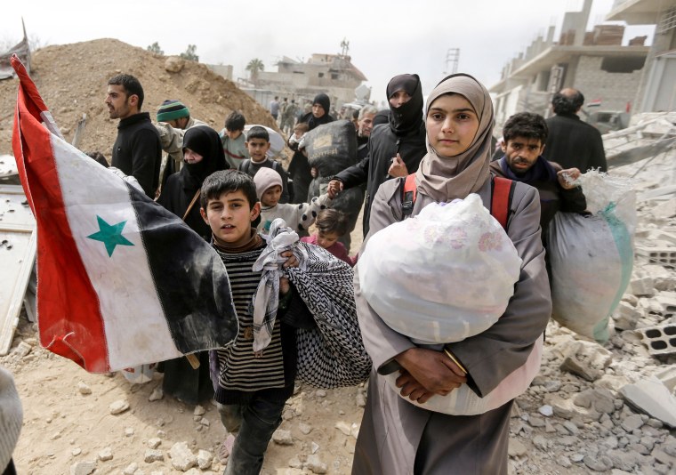 Image: A Syrian child walks with a national flag with other civilians evacuated