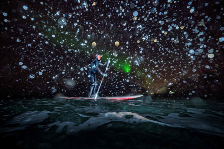 Image: Myrtille Heissat rides a stand up paddle board under Northern Lights in Unstad