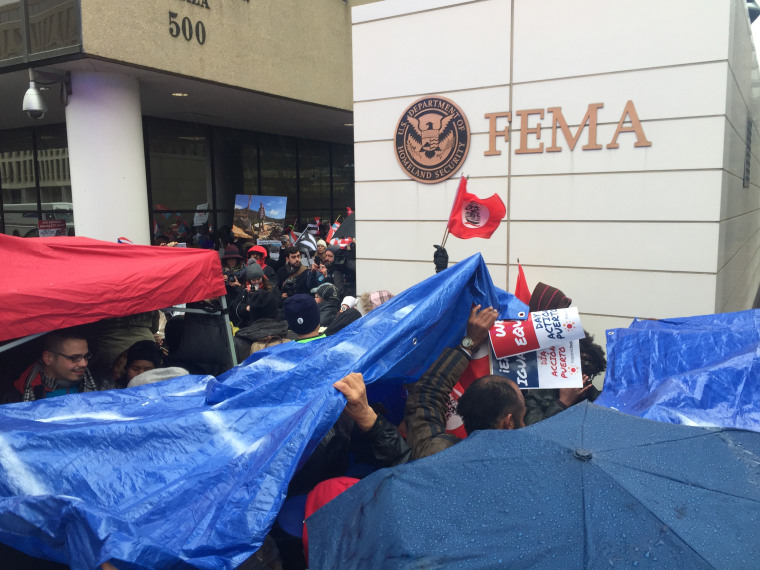 Crowds gather in front of the FEMA building in D.C. with blue tarps, symbolizing the same blue tarps that still cover homes in Puerto Rico six months after Hurricane Maria.