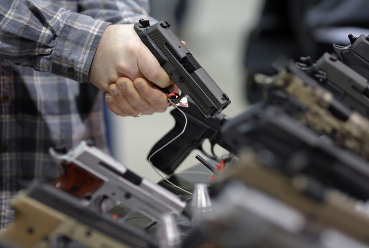 Image: A visitor holds a pistol at a gun display during a National Rifle Association outdoor sports trade show