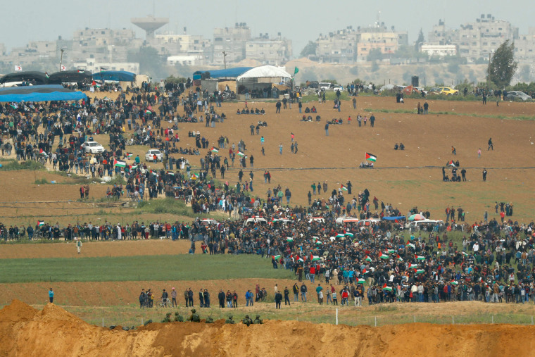 Palestinians participate in the tent city protest commemorating Land Day, with Israeli soldiers watching from across the border.