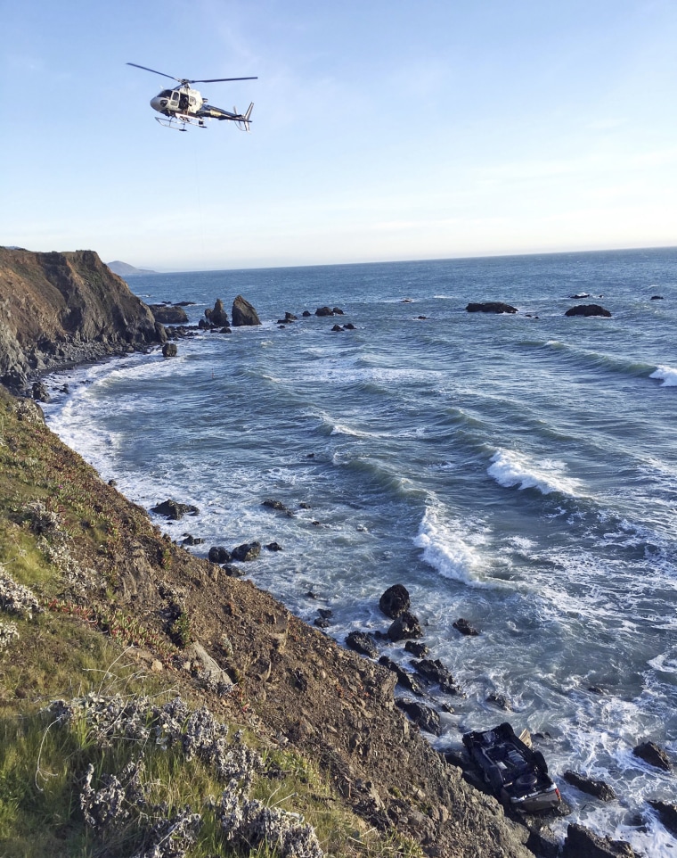 Image: A helicopter hovers over steep coastal cliffs at the scene of a car crash