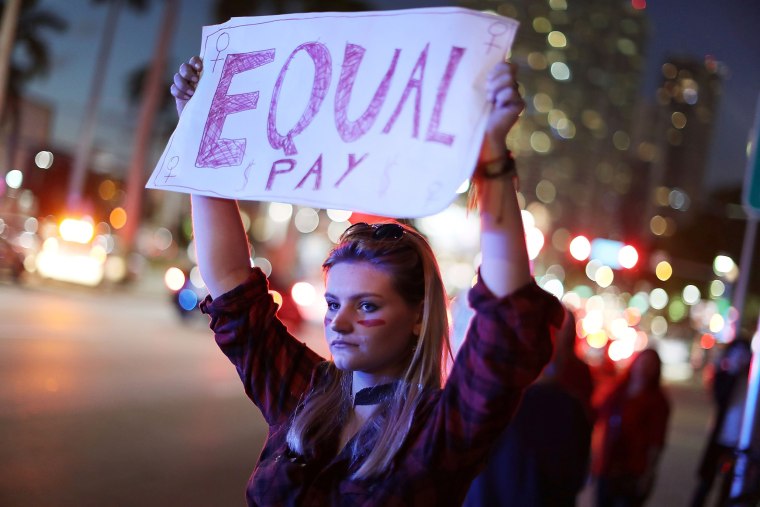 Image: A women holds a sign reading 'Equal Pay'