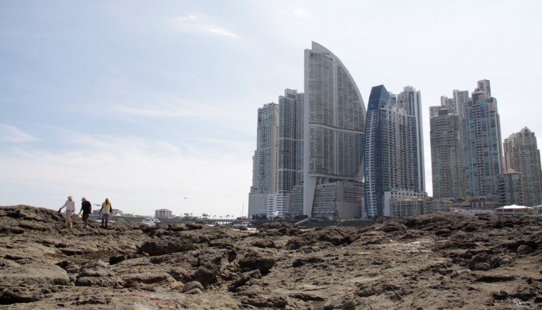 Image: People stand on rocks on the shore during low tide as the Trump Ocean Club International Hotel and Tower Panama is seen next to apartment buildings in Panama City