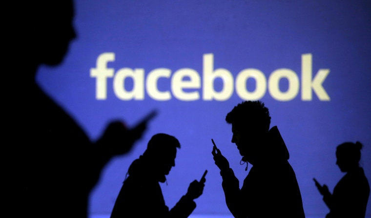 Image: mobile users are seen next to a screen projection of Facebook logo in this picture illustration