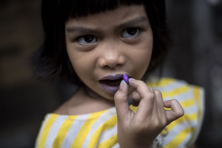 Image: A child uses a candy to color her lips in Manila