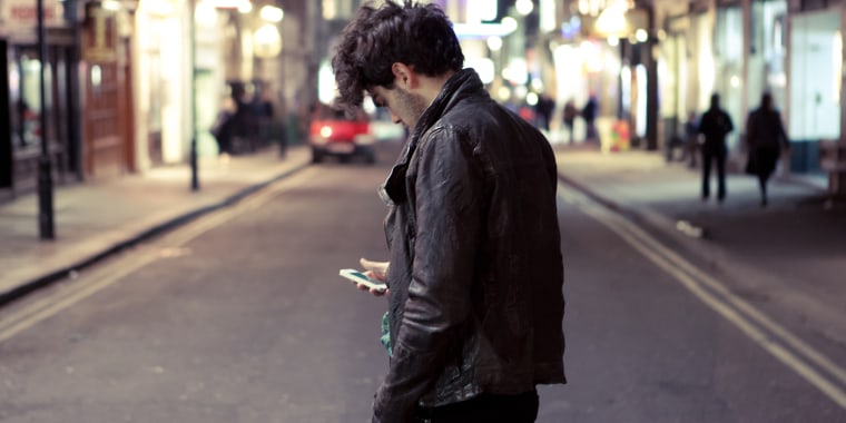 Young man checks phone as he crosses the road