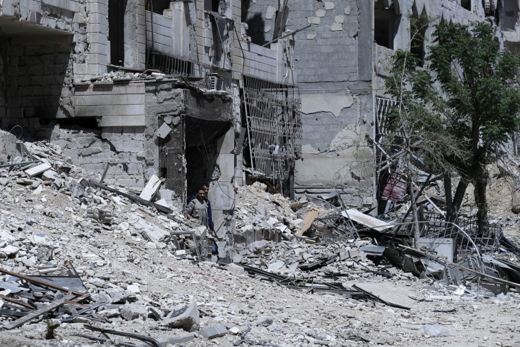 Image: Syrians walk through destruction in the town of Douma, the site of a suspected chemical weapons attack, near Damascus