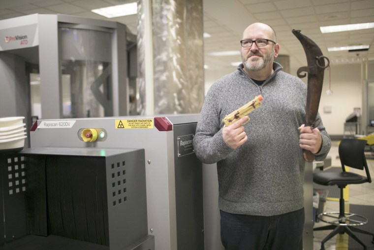 Image: Bob Burns, a TSA public affairs specialist and the agency's social media lead, poses with confiscated weapons at the Dayton International Airport in Dayton, Ohio on April 28, 2018.
