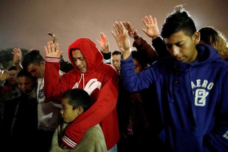 Image: Members of a caravan of migrants from Central America, pray near the San Ysidro checkpoint after the first fellow migrants entered U.S. territory to seek asylum on Monday, at improvised shelter in Tijuana