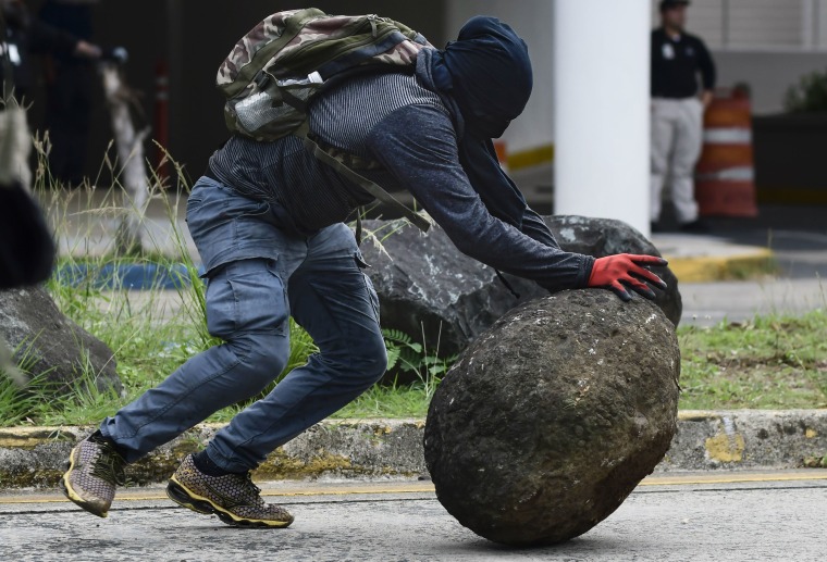 Image: A masked protester pushes a boulder during protests