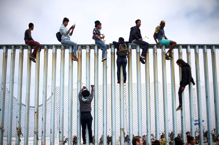 Image: Members of a caravan of migrants from Central America climb up the border fence between Mexico and the U.S., as a part of a demonstration prior to preparations for an asylum request in the U.S., in Tijuana