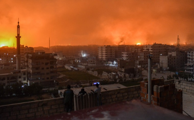 Image: People watch explosions over the skyline of the Syrian capital of Damascus