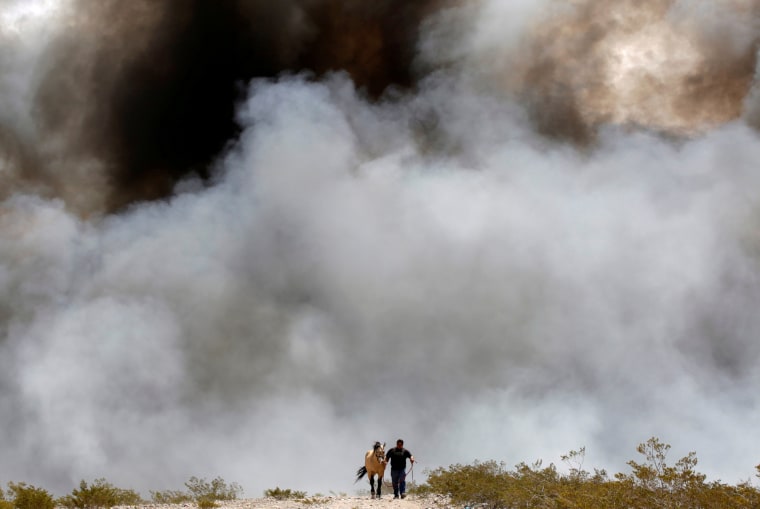 Image: A man evacuates his horse from the area as the fire burns through a pile of old tyres at a recycling centre in Ciudad Juarez