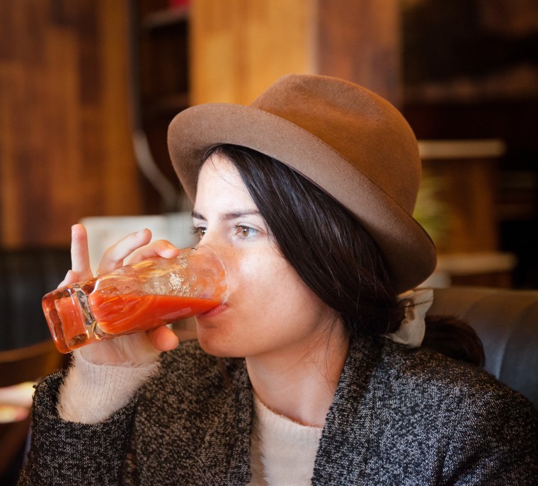 quirky girl with trilby hat enjoys tomato juice in cafe