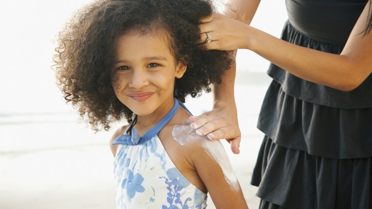 Hispanic mother rubbing sunscreen on daughter at beach