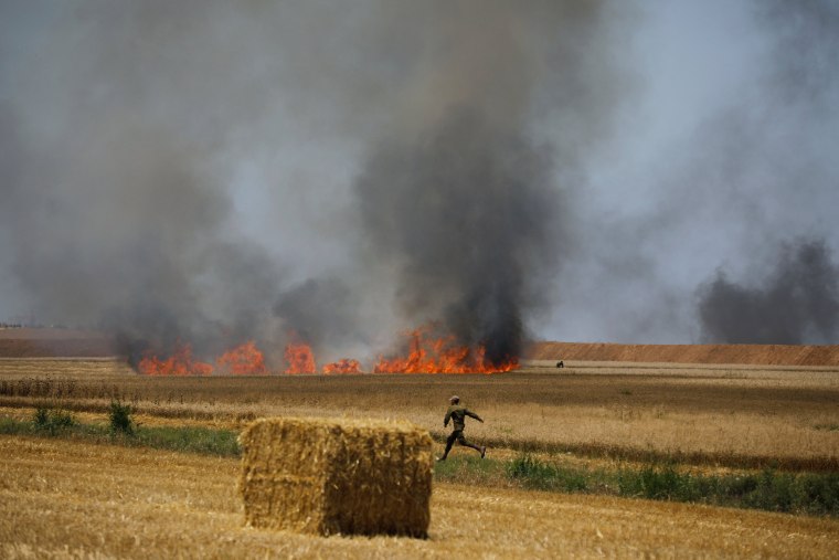 Image: An Israeli soldier runs in a field which has caught fire, close to the Israeli side of the border fence between Israel and Gaza near kibbutz Mefalsim