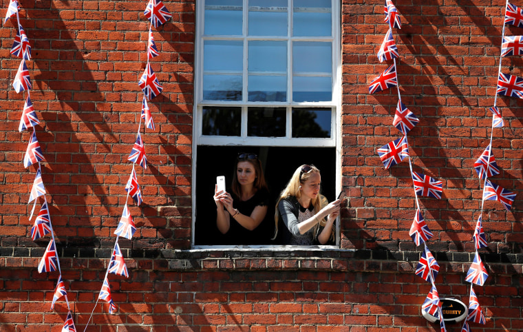 Image: Women take photos on their smartphones as they lean out of the window of a building near Windsor Castle in Windsor