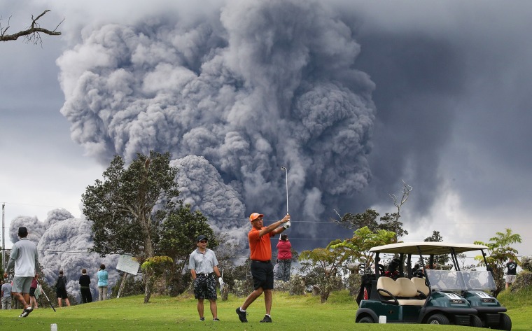 Image: An ash plume from the Kilauea volcano rises in the distance behind golfers
